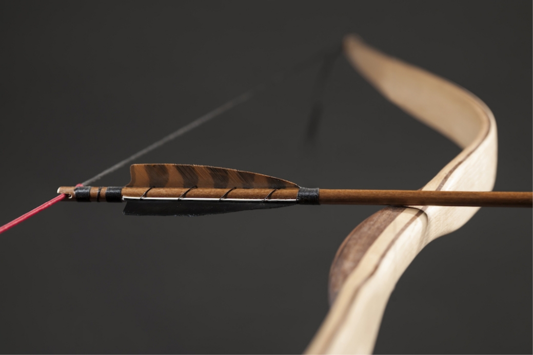 Porträtaufnahme eines Holzbogens mit Pfeil auf dunklem Hintergrund